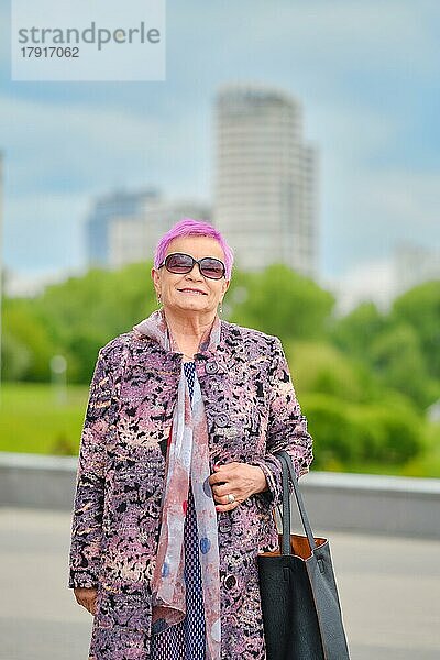 Urbanes Porträt einer fröhlichen alten Frau mit rosa Haaren und Kaschmirmantel