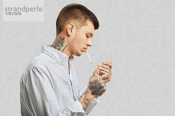 Junger tätowierter Mann zündet sich im Studio eine Zigarette an