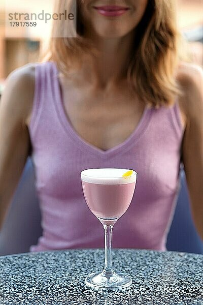 Unbekanntes Mädchen hinter dem Tisch mit Kirschschnaps-Cocktail auf der Terrasse (Weichzeichner-Foto)