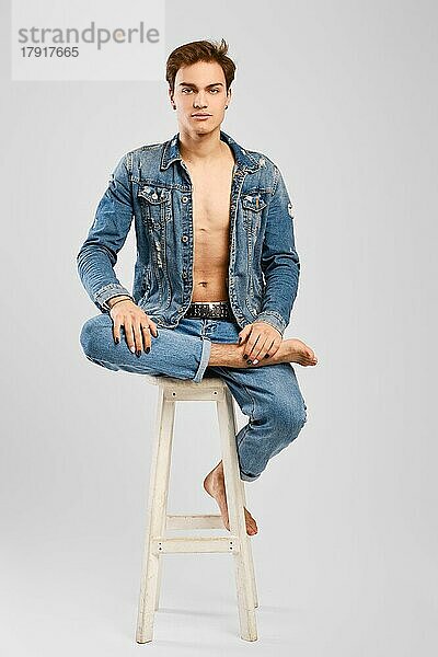 Junger Mann in Jeanskleidung sitzt auf einem hohen Stuhl