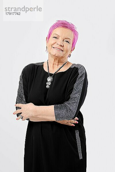 Lächelnde alte Frau mit kurzen rosa Haaren hält die Hände gekreuzt. Positive Emotion Konzept