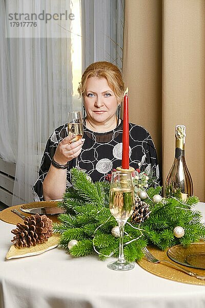 Fröhliche Frau mittleren Alters  die Weihnachten feiert und hinter dem festlichen Tisch sitzt
