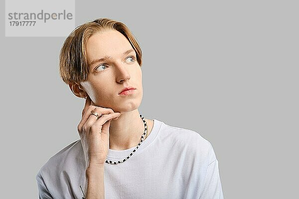 Closeup-Porträt eines nachdenklichen jungen Mannes im weißen T-Shirt vor grauem Studiohintergrund