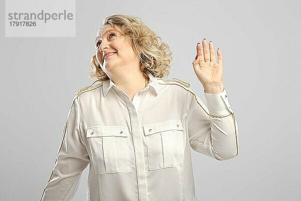 Ältere Frau winkt ungläubig mit der Hand vor grauem Hintergrund