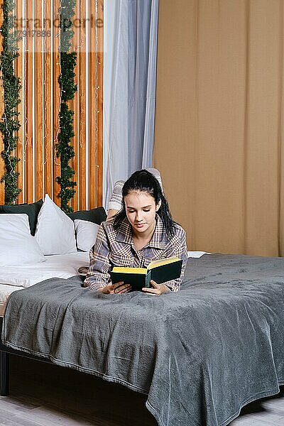 Clevere junge Frau  die im Urlaub im Bett ein Buch liest