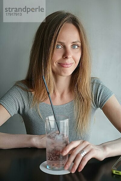 Weichzeichner Porträt von hübschen jungen Mädchen hinter dem Tisch mit kalten Cocktail