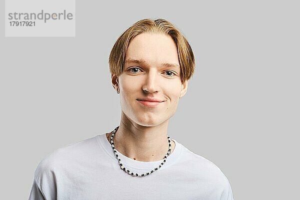 Closeup-Porträt eines lächelnden jungen Mannes im weißen T-Shirt vor grauem Studiohintergrund