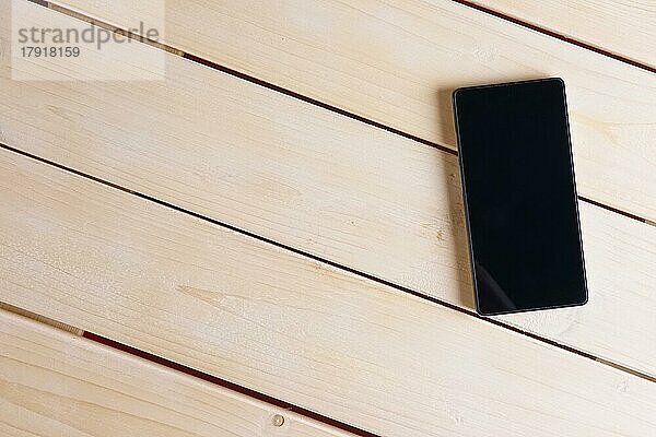 Draufsicht auf ein Smartphone auf einem leeren Holztisch