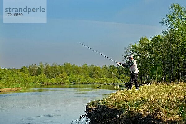 Mann fischt mit Spinning am Flussufer  wirft Köder. Wochenendaktivität im Freien. Foto mit geringer Schärfentiefe bei weit geöffneter Blende aufgenommen