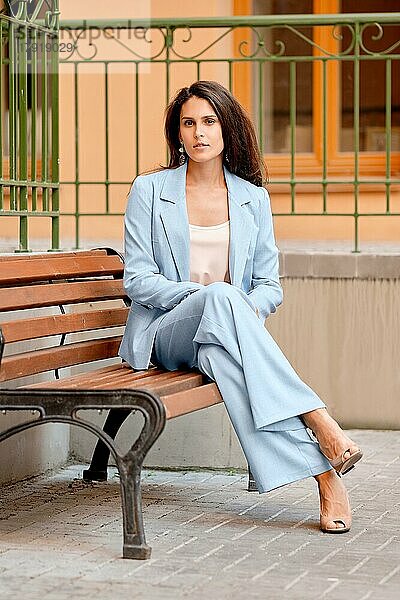 Stilvolle Frau im himmelblauen Hosenanzug  die sich auf einer Bank in der Nähe des Büros ausruht