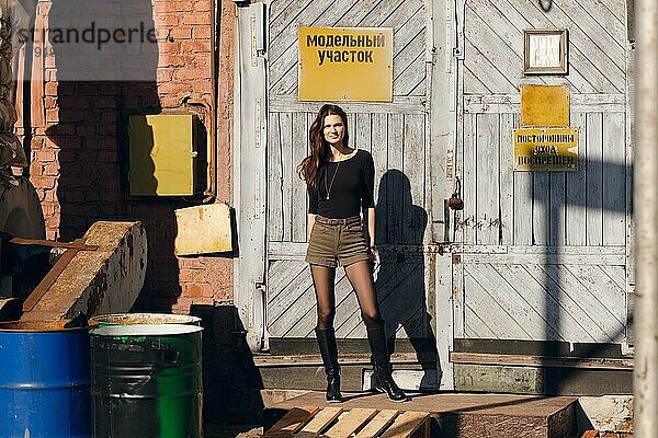 Foto eines attraktiven Mädchens  das vor einem Fabriktor mit Warnschild posiert. (Aufschrift auf dem Schild ist auf Russisch kann als Modellbereich und nicht betreten übersetzt werden)