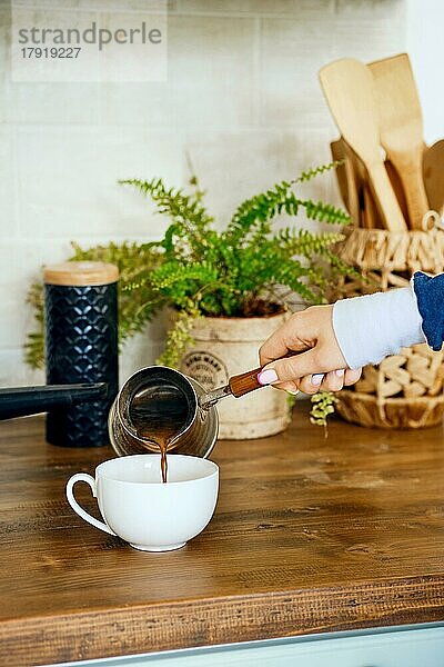 Nahaufnahme einer Hand  die Kaffee in eine Tasse gießt. Morgen Routine Konzept