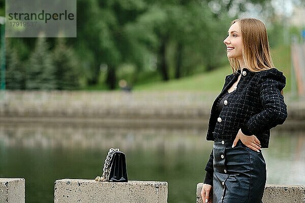Junge fröhliche Frau posiert im Freien mit einem Fluss im Hintergrund