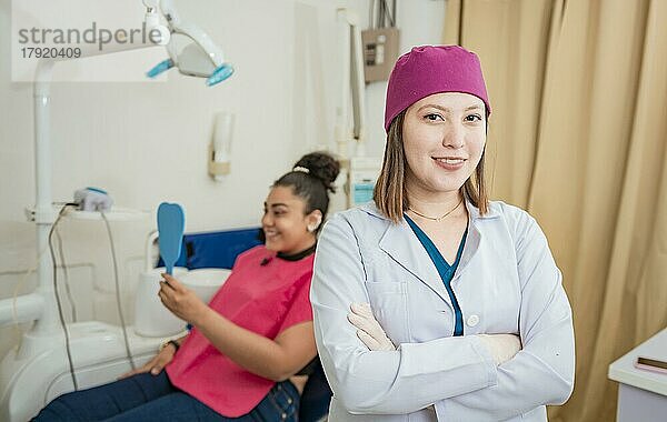 Porträt eines Zahnarztes mit verschränkten Armen vor einem Patienten  Lächelnde Zahnärztin in einer Klinik  Porträt einer jungen Zahnärztin in einer modernen Zahnklinik. Nahaufnahme einer Zahnärztin mit verschränkten Armen