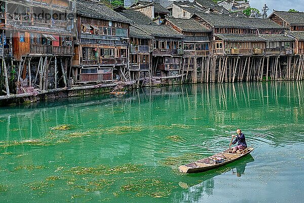 FENGHUANG  CHINA  23. APRIL 2018: Nicht identifizierter chinesischer Mann im Boot Feng Huang Ancient Town (Phoenix Ancient Town) am Tuo Jiang Fluss mit Brücke und Touristenboot. Provinz Hunan  China  Asien