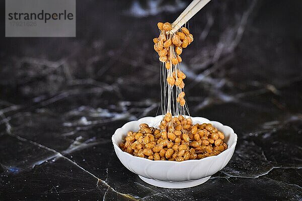 Traditionelles japanisches Lebensmittel Natto aus fermentierten Sojabohnen Zeichnung klebrige Fäden auf Stäbchen auf dunklem Hintergrund