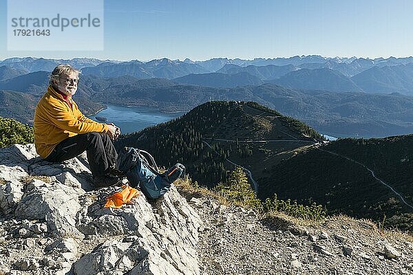 Wanderer  Senior  64  hält Rast am Gipfel des Herzogstand und genießt die Aussicht auf Fahrenbergkopf  Walchensee  Rofan und Karwendelgebirge  Walchensee  Bayerische Voralpen  Oberbayern  Deutschland  Europa