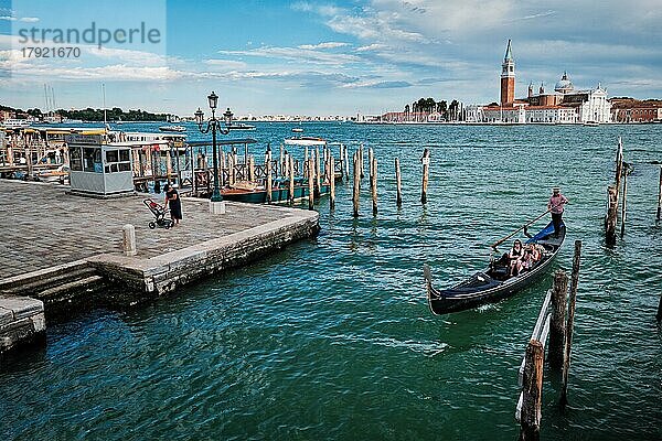 VENEDIG  ITALIEN  27. JUNI 2018: Gondoliere mit Touristen in einer Gondel in der Lagune von Venedig am Markusplatz mit der Kirche San Giorgio di Maggiore im Hintergrund in Venedig  Italien  Europa