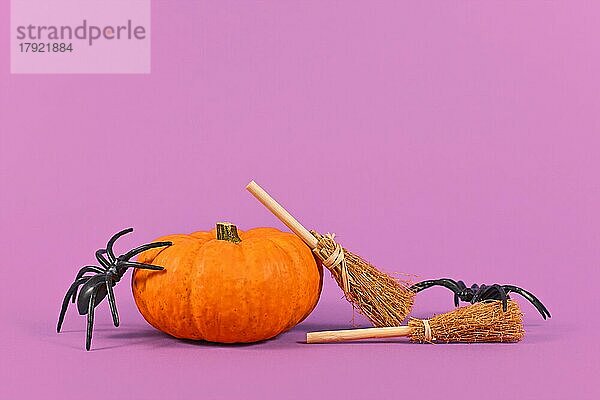 Orange Kürbis mit Halloween Spinnen und Besen auf violettem Hintergrund mit Kopie Raum