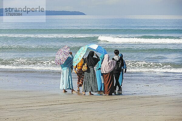 Muslimische Frauen und ein junger Mann schauen am Strand von Bali  Indonesien  ins Meer  Asien