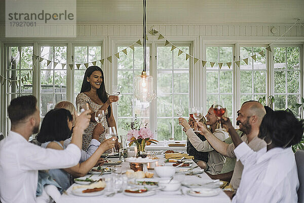 Lächelnde Frau stößt mit Familienmitgliedern auf ein Getränk während einer Dinnerparty zu Hause an