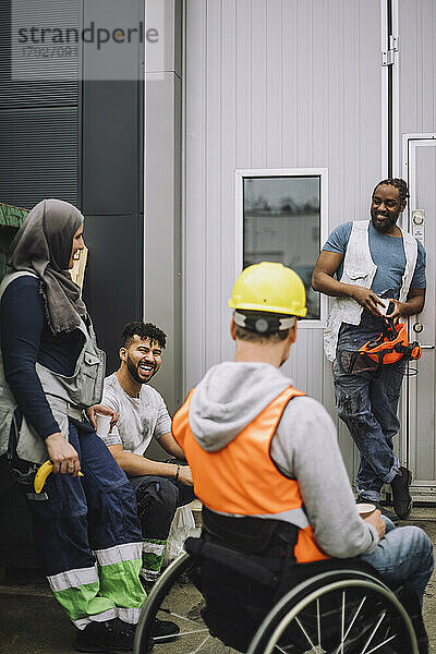 Glücklicher junger Bauarbeiter im Gespräch mit männlichen und weiblichen Kollegen während einer Pause auf der Baustelle