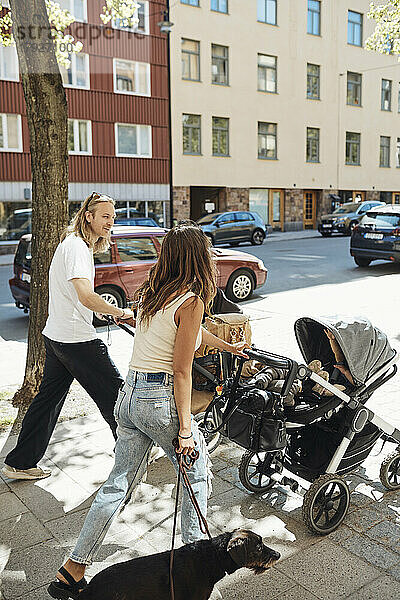 Mann und Frau unterhalten sich  während sie Kinderwagen mit Kindern auf dem Gehweg schieben