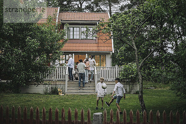 Jungen spielen Fußball im Hinterhof  während die Familie auf der Veranda eine Party feiert