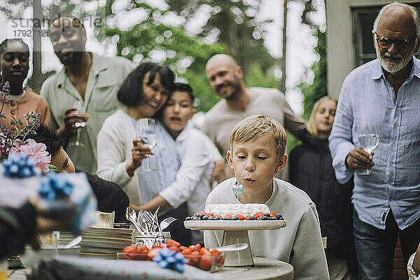 Junge bläst Kerze auf Kuchen während Geburtstagsfeier mit Familie