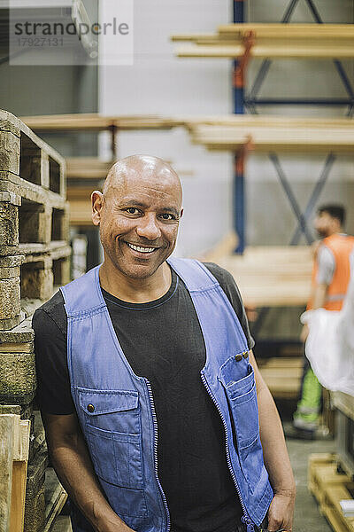 Glücklicher glatzköpfiger Zimmermann  der sich auf ein Holzregal im Lagerhaus stützt