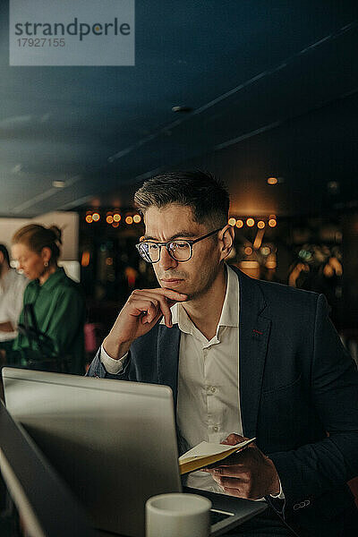 Geschäftsmann mit Hand am Kinn  der auf einen Laptop schaut  während er im Hotel sitzt