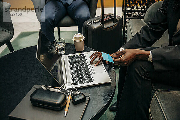 Junge Geschäftsfrau hält eine Kreditkarte in der Hand und benutzt einen Laptop in einer Hotel-Lounge
