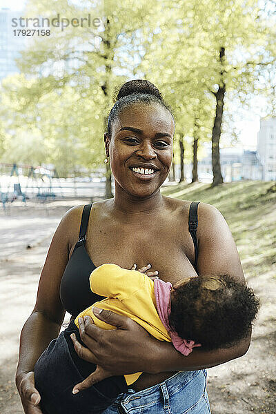 Porträt einer glücklichen Frau  die ihre Tochter im Park stillt