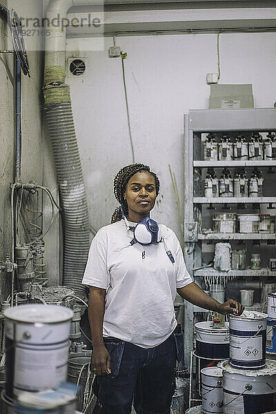 Porträt einer selbstbewussten Malerin  die in einer Werkstatt neben einer Farbdose steht