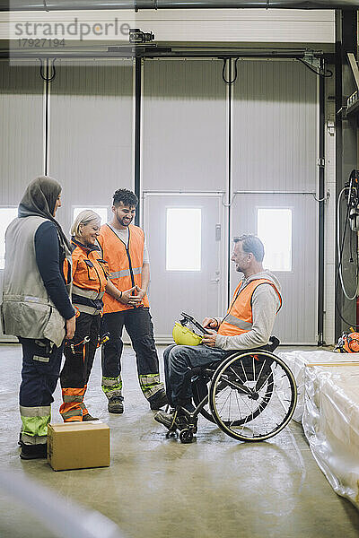 Zimmermann im Rollstuhl sitzend  der mit einem männlichen und einem weiblichen Kollegen im Lagerhaus diskutiert