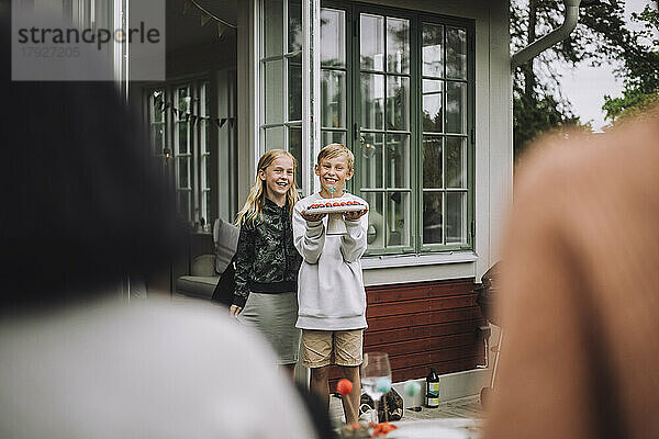 Junge hält Kuchen  während er mit einem weiblichen Geschwisterkind in der Nähe der Tür steht
