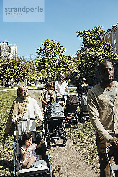 Eltern gehen spazieren  während Kinder in Kinderwagen im Park an einem sonnigen Tag
