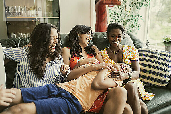Glückliche Mutter und Töchter spielen mit Jungen  während sie zu Hause auf dem Sofa sitzen