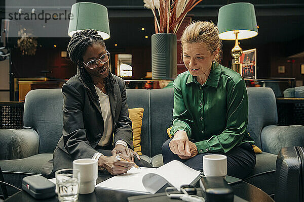 Junge Geschäftsfrau im Gespräch mit einer Kollegin bei der Vertragsunterzeichnung in einer Hotelhalle