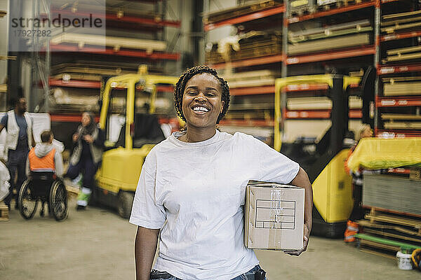Porträt eines glücklichen Schreiners mit Karton im Lagerhaus