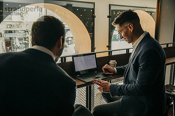 Geschäftsmann  der seinen Laptop mit einem männlichen Kollegen teilt  während er in einer Hotellounge sitzt