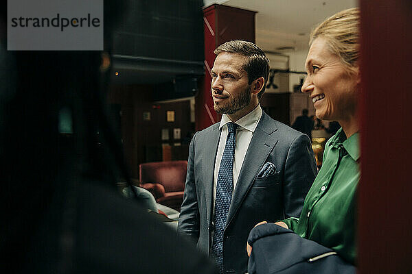 Lächelnde reife Geschäftsfrau steht neben einem männlichen Fachmann in einer Hotelhalle
