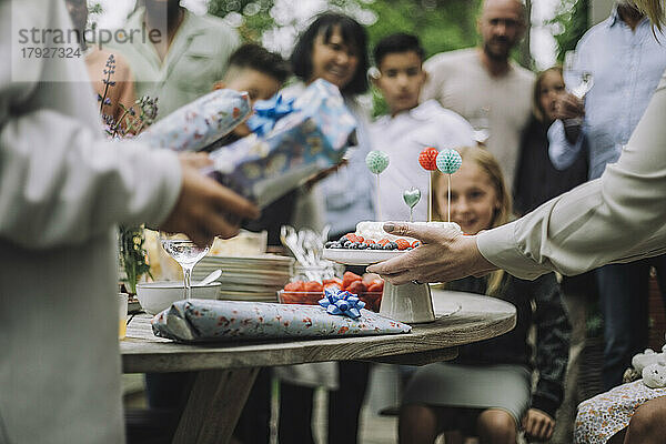 Hände einer Frau halten einen dekorierten Geburtstagskuchen auf dem Tisch