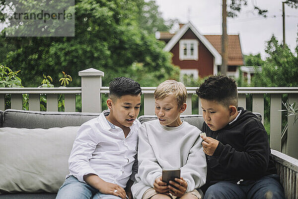 Aufgeregte Jungen teilen sich ihr Smartphone  während sie zusammen auf der Couch sitzen