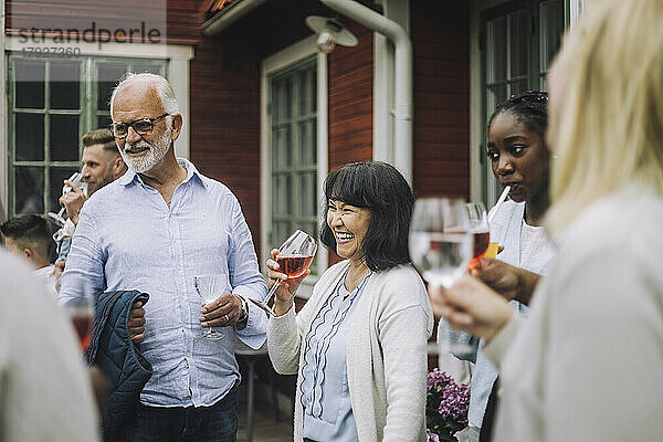 Glückliche Frau mit Weinglas in der Hand und Familie bei geselligem Beisammensein