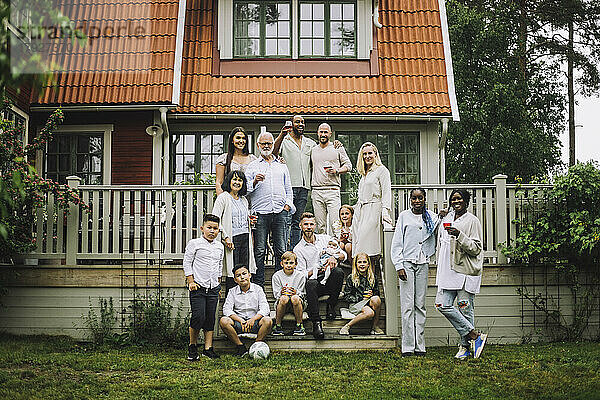 Mehrgenerationenfamilie mit Weinglas posiert auf der Veranda vor dem Haus