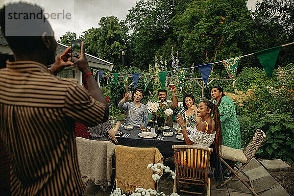 Mann fotografiert männliche und weibliche Freunde mit dem Smartphone bei einer Gartenparty