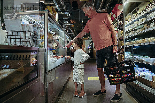 Älterer Mann zeigt seinem Enkel beim Einkaufen im Supermarkt Lebensmittel in der Auslage