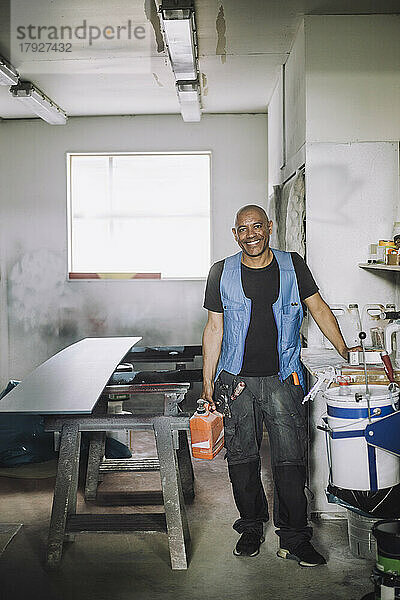 Ganzkörperporträt eines lächelnden männlichen Malers in einer Werkstatt
