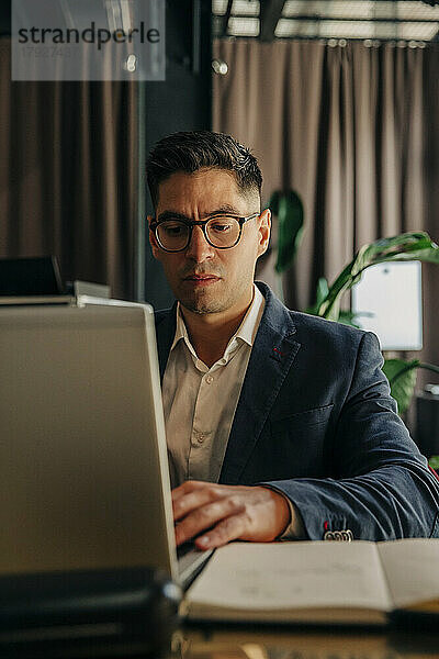 Mittlerer erwachsener Geschäftsmann mit Brille  der einen Laptop benutzt  während er in einer Hotel-Lounge sitzt